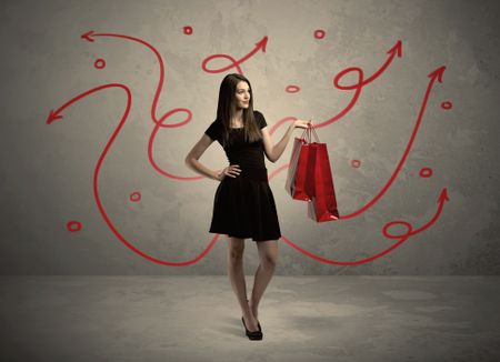 An elegant young lady in black holding red shopping bags in front of urban wall background with drawn red arrows and circles concept