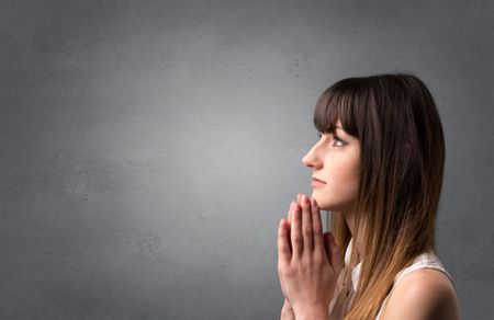 Young woman praying on a grey background