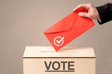 Close up of male hand putting vote into a ballot box, on grunge background