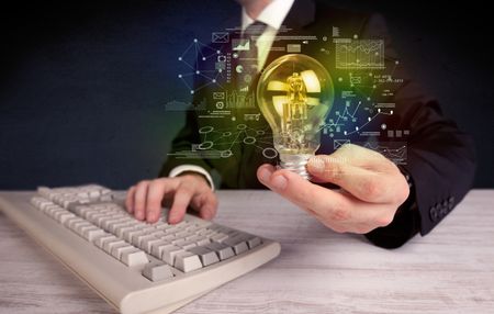 A serious business person has a complex solution concept illustrated by glowing glass light bulb in his hand with graph charts, numbers, lines, calculations.