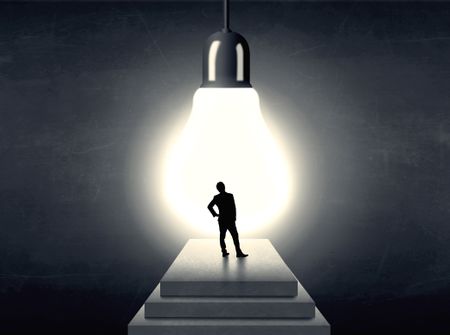 Businessman standing on a step in front of a huge light bulb, concept of having an idea.