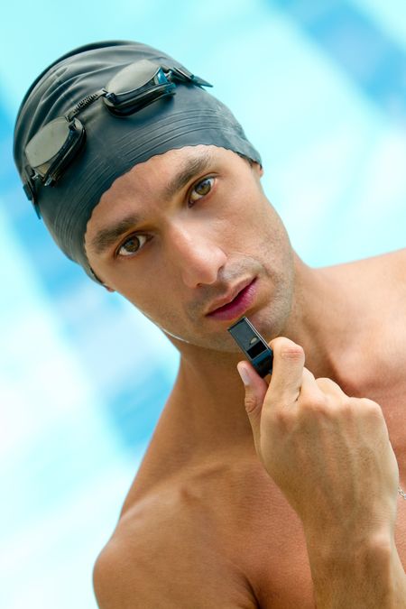 Male lifeguard at the swimming pool holding a whistle