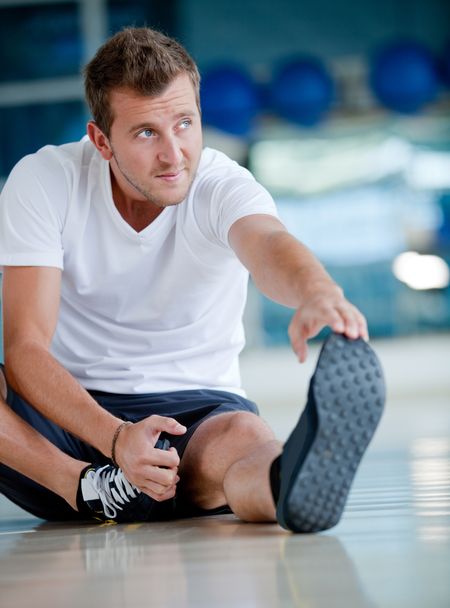 Man at the gym doing stretching exercises and smiling on the floor
