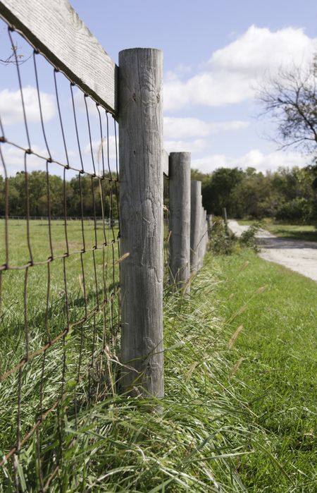 Farm fence by dirt road in American Midwest (shallow depth of field; focus on post in foreground)