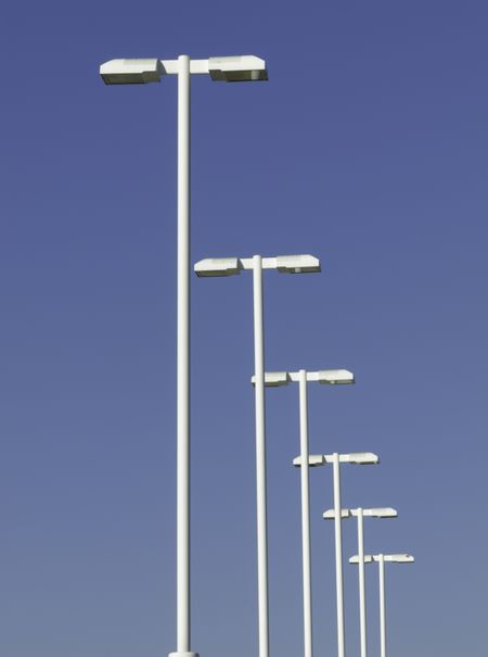 Row of tall white lampposts over parking lot, with background of blue sky