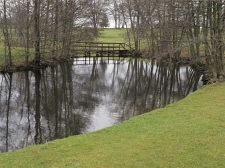 Public golf course on a winter day without snow, northern Illinois: Bend in stream reflecting bare trees by footbridge