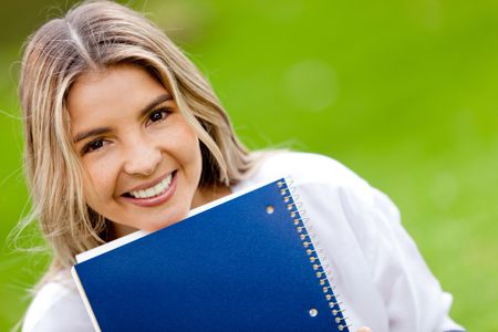 Beautiful female student holding notebooks outdoors and smiling