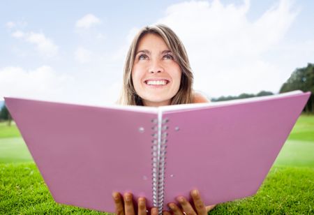 Thoughtful female student holding a notebook and smiling outdoors
